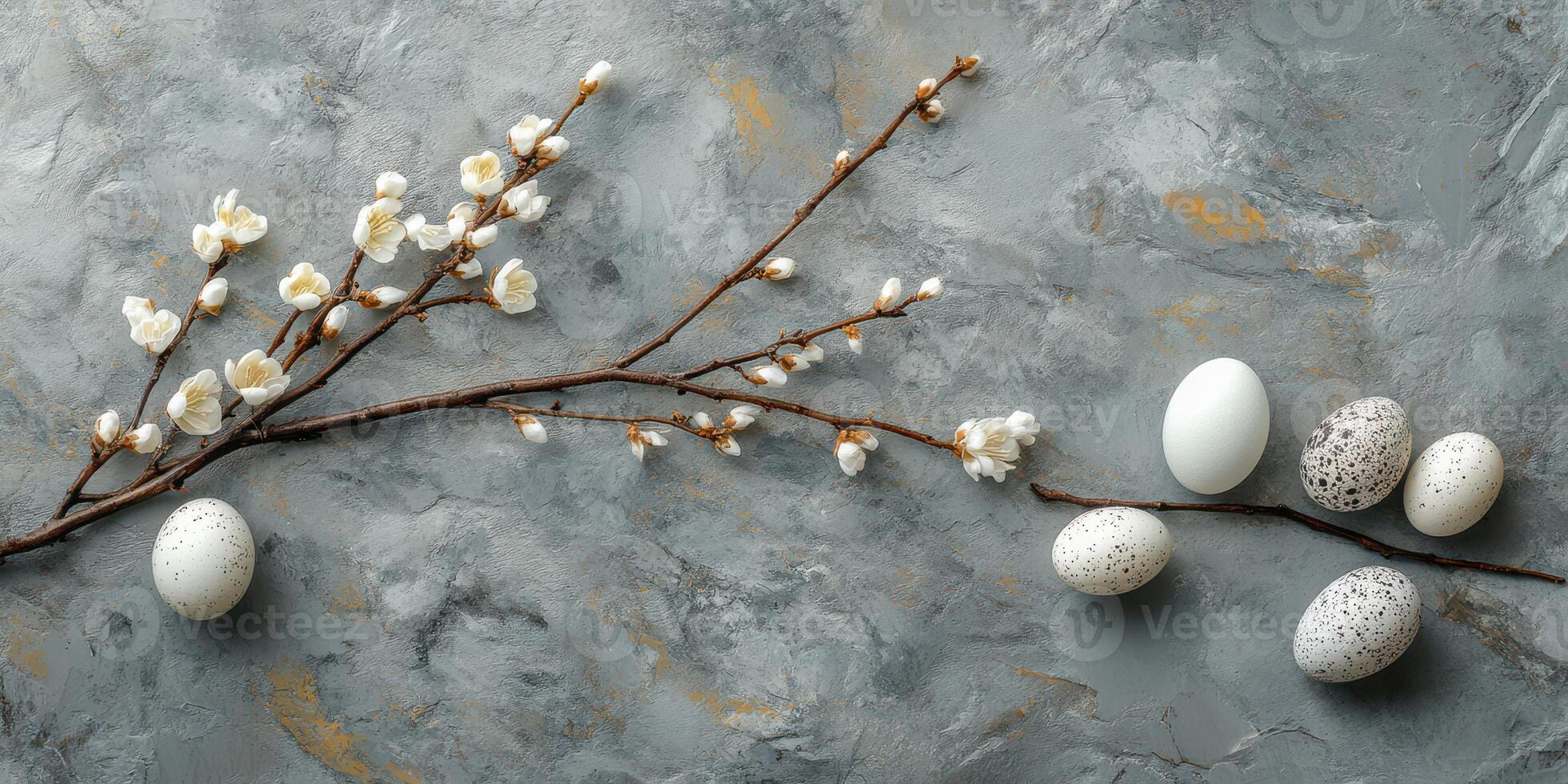 Decorative branch with flowers and assorted eggs laid on a textured gray surface for a spring celebration photo