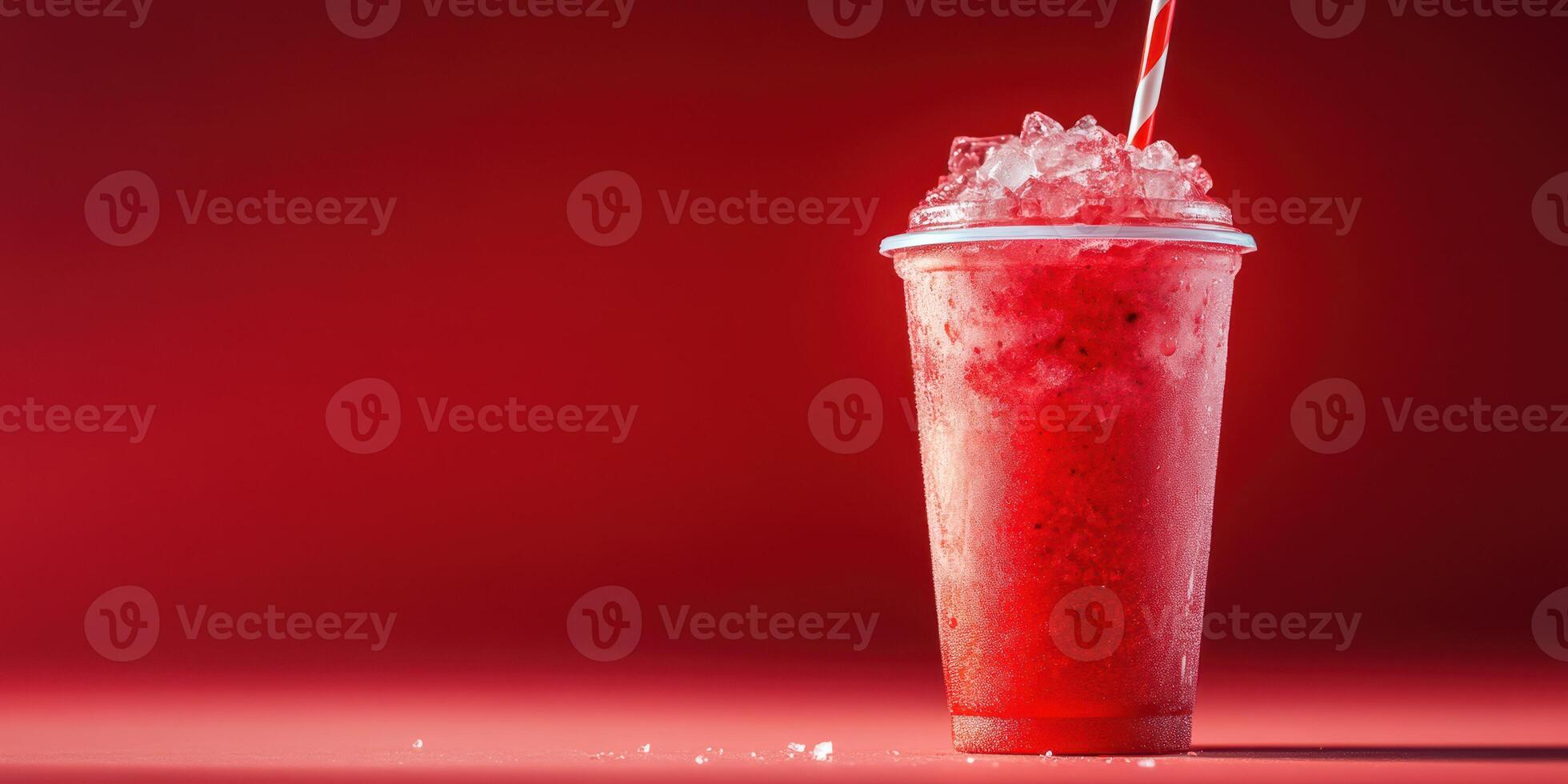 Refreshing frozen drink served in a clear cup with ice and a straw against a vibrant red background photo
