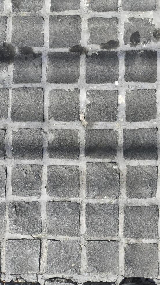 image features textured gray cobblestone pavement with grid pattern, showcasing unique surface details and shadows photo