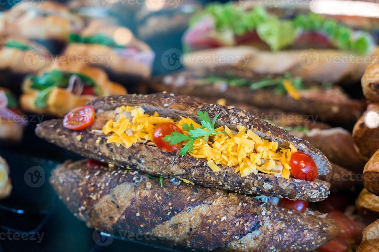 Fresh whole grain panini sandwich with cheddar cheese and cherry tomatoes in a bakery display. photo