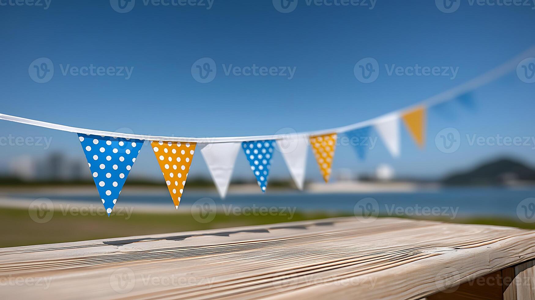 Colorful bunting flags decorate a wooden table by the seaside, with a clear blue sky and distant hills photo