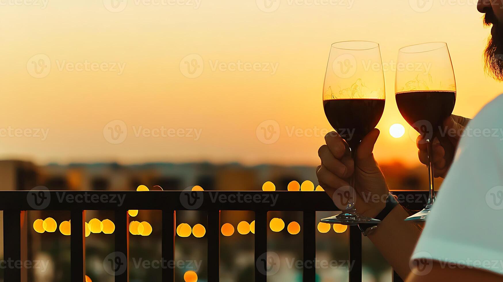 Couple toasting with wine glasses at sunset on a balcony, city skyline blurred in background photo