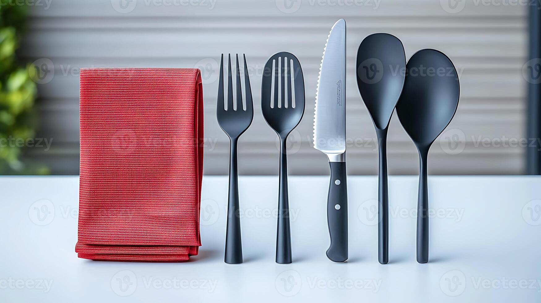Stylish black cutlery set arranged neatly beside a red napkin on a clean table, with greenery in background photo