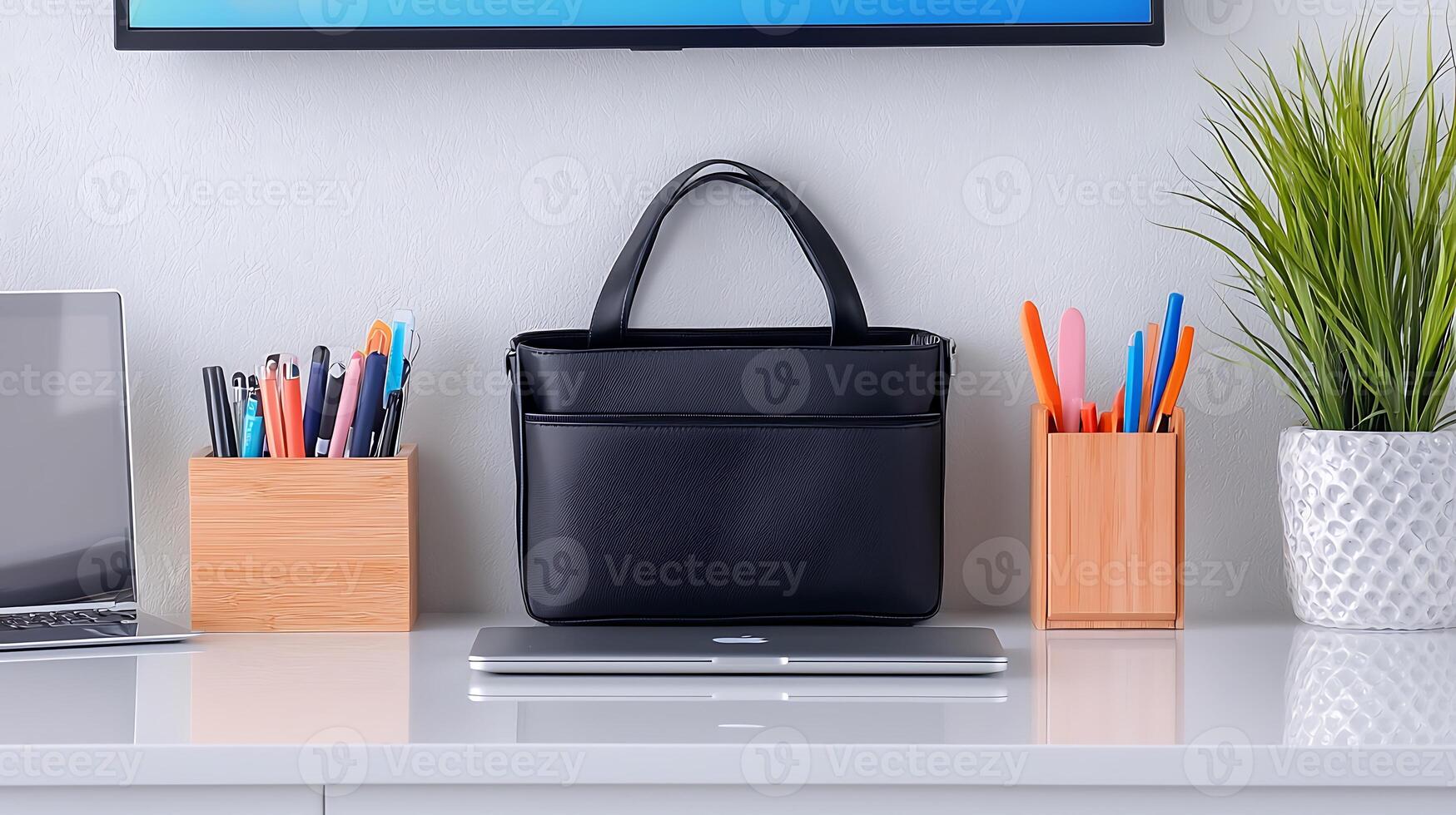 Stylish black handbag placed on a desk with stationery and a laptop, in a modern workspace photo