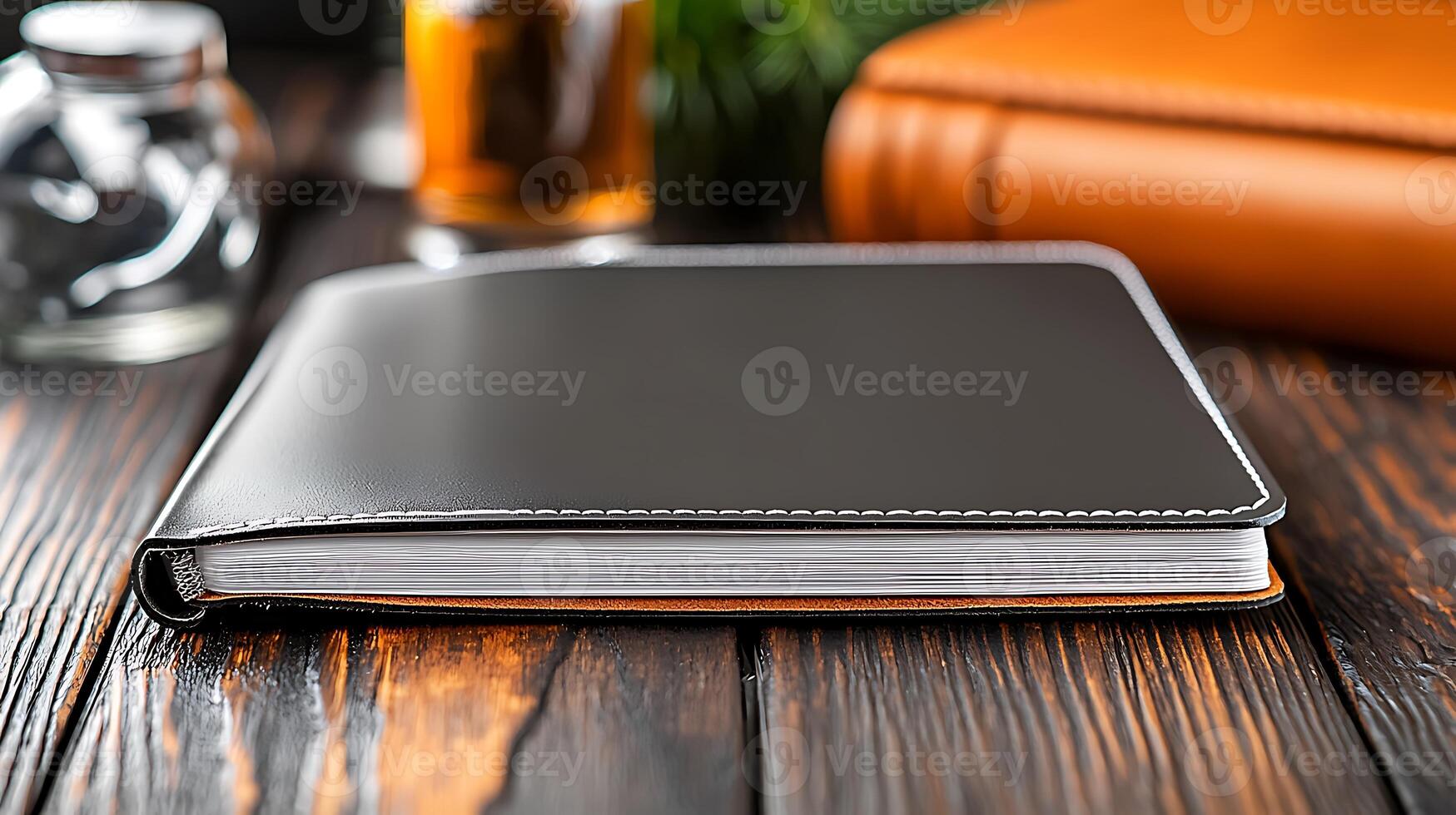 Stylish black notebook resting on a wooden table beside a glass of iced tea and leather-bound journal photo