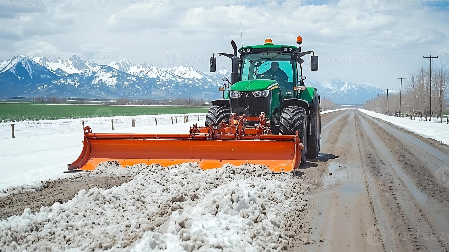Tractor clearing snow from a rural road with mountains in the background on a sunny day photo