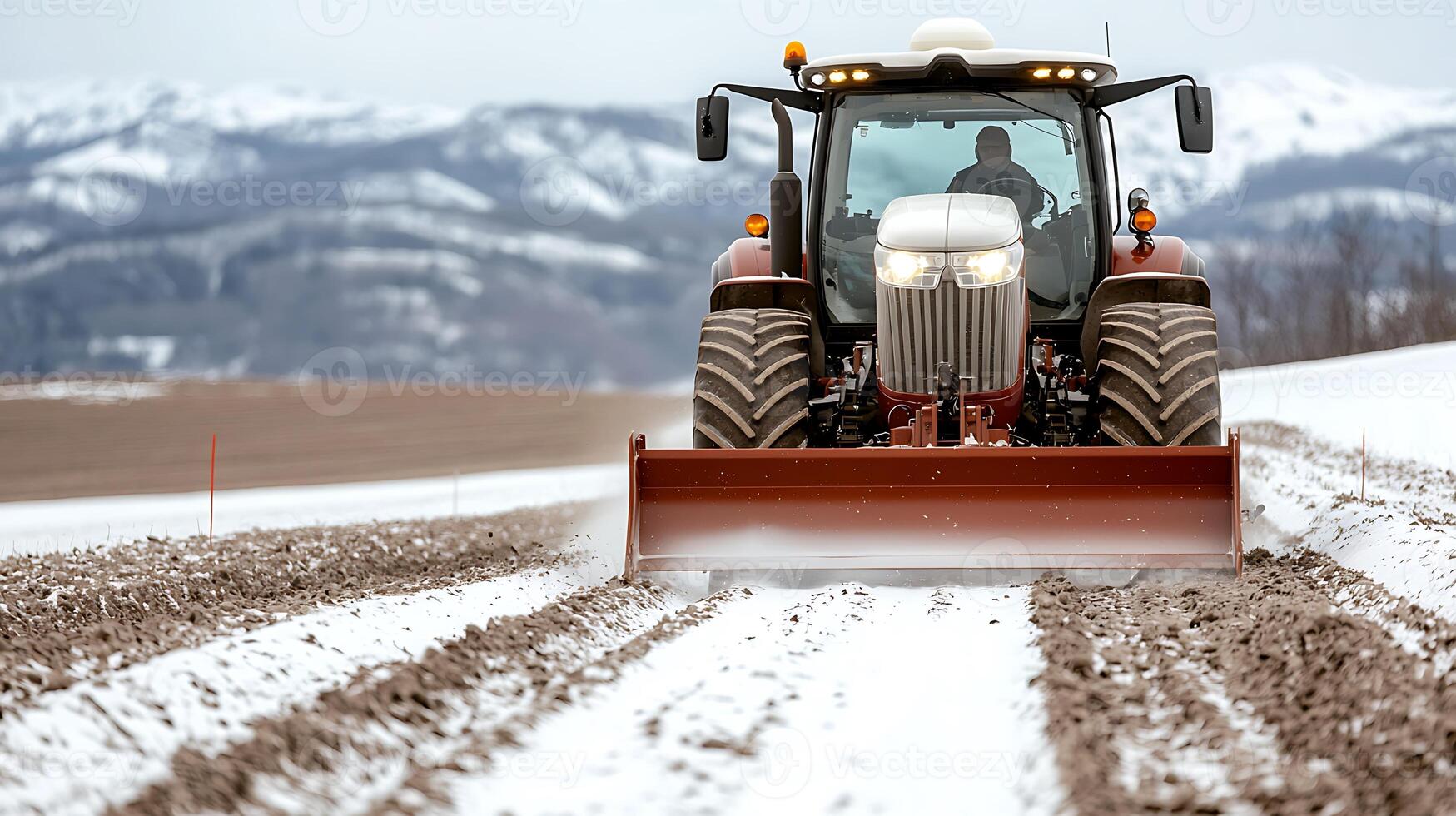 Tractor plowing snowy field in mountainous landscape, preparing soil for spring planting photo