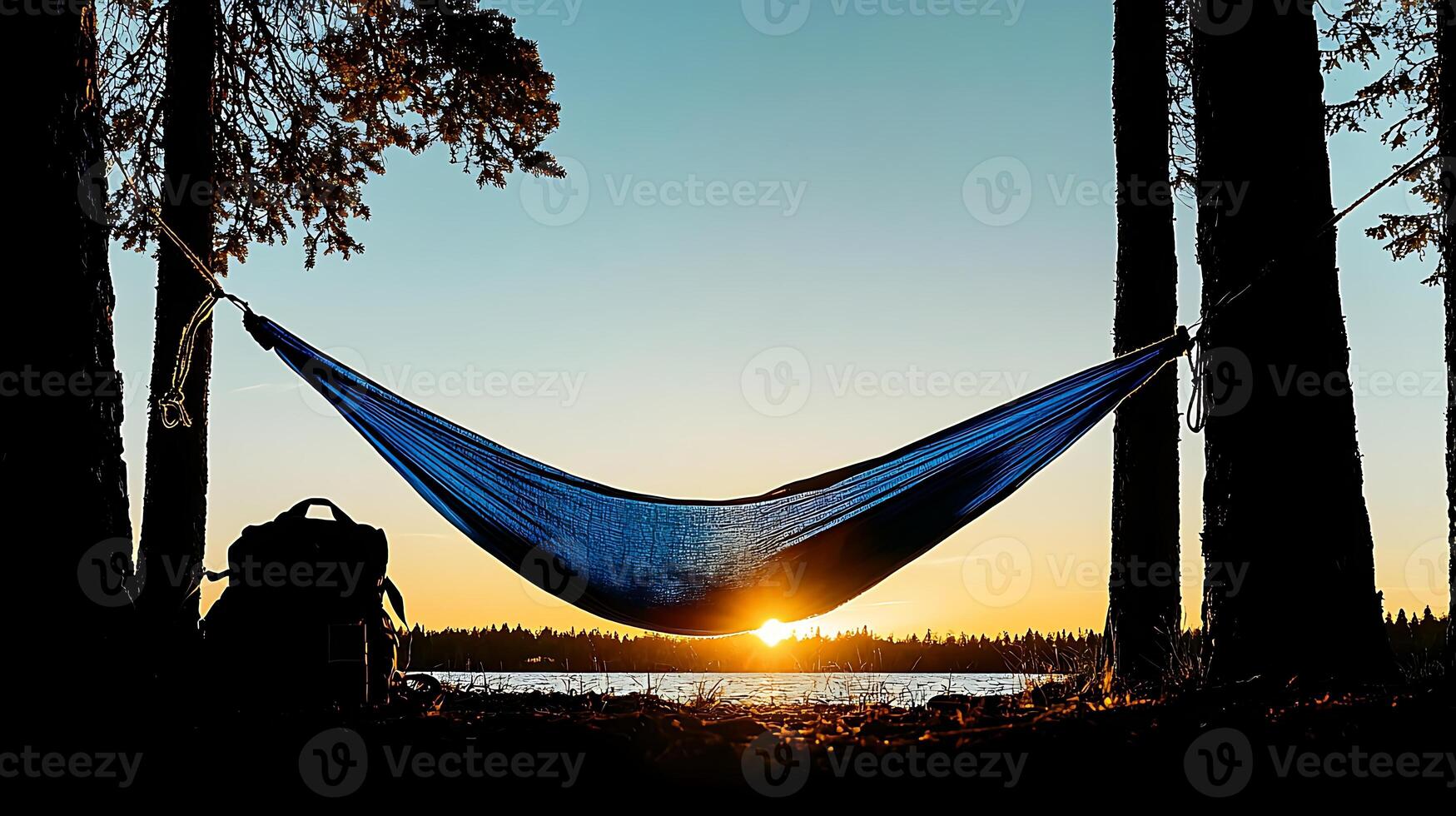 Tranquil sunset view with a hammock between trees and a backpack by a serene lakeside photo