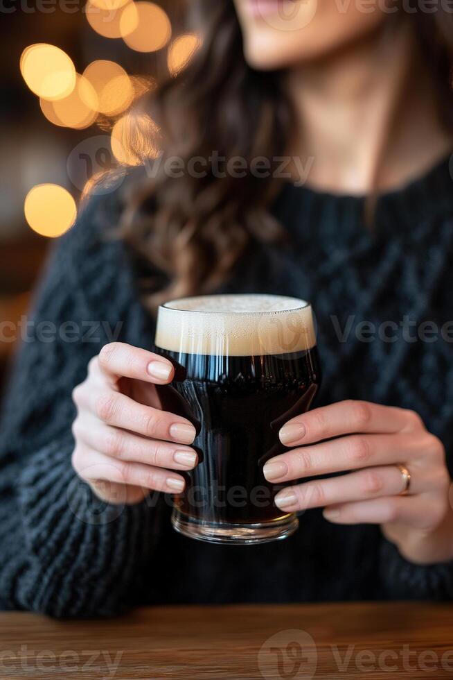 A woman relaxes in a traditional Irish pub, gently sipping her pint of stout beer. The warm ambiance features rustic wood accents and glowing lights, creating a welcoming atmosphere photo