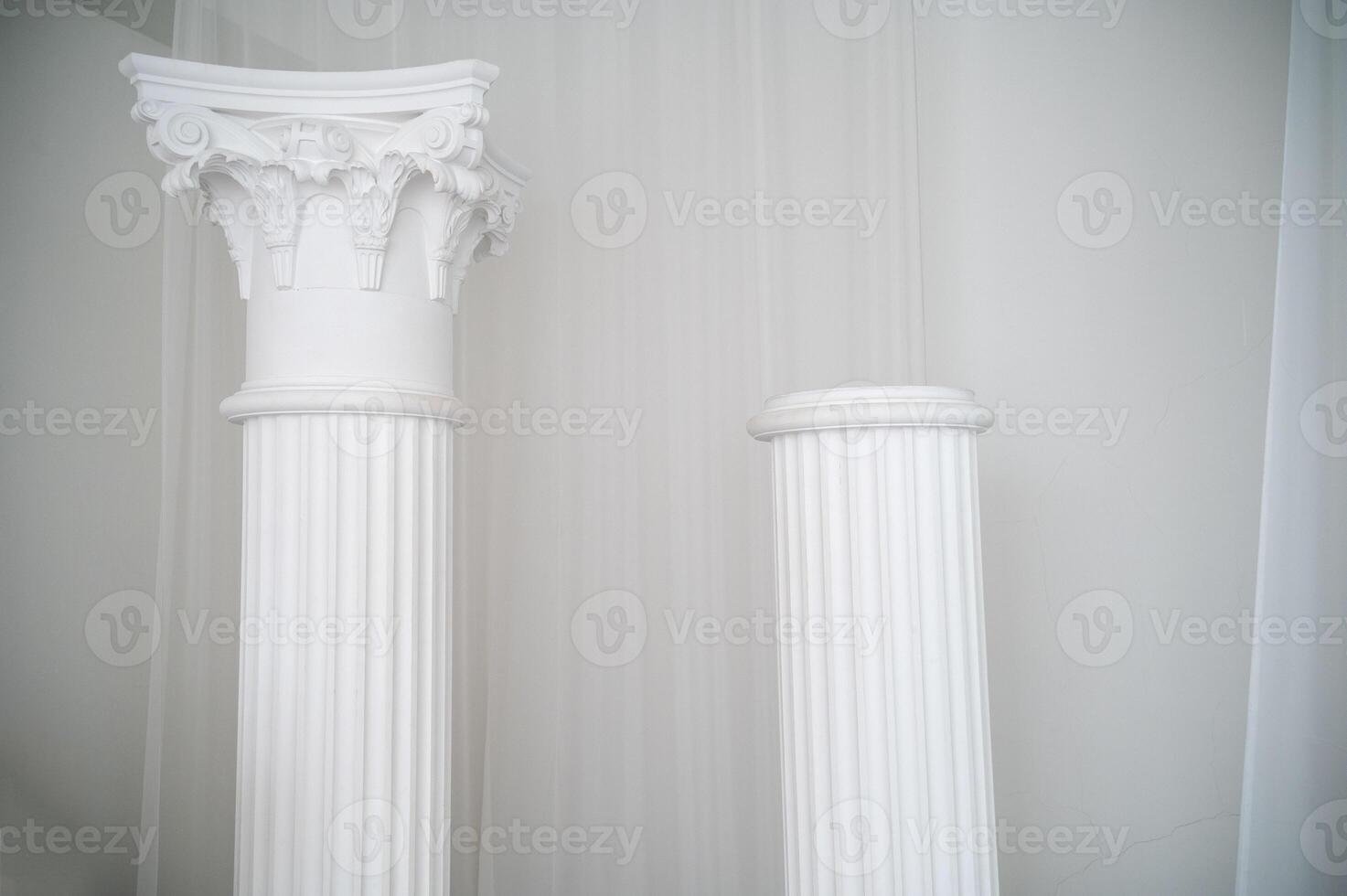 element of antique column in interior. photo zone for photo sessions. two white columns are located in interior. white chiffon fabric is planted