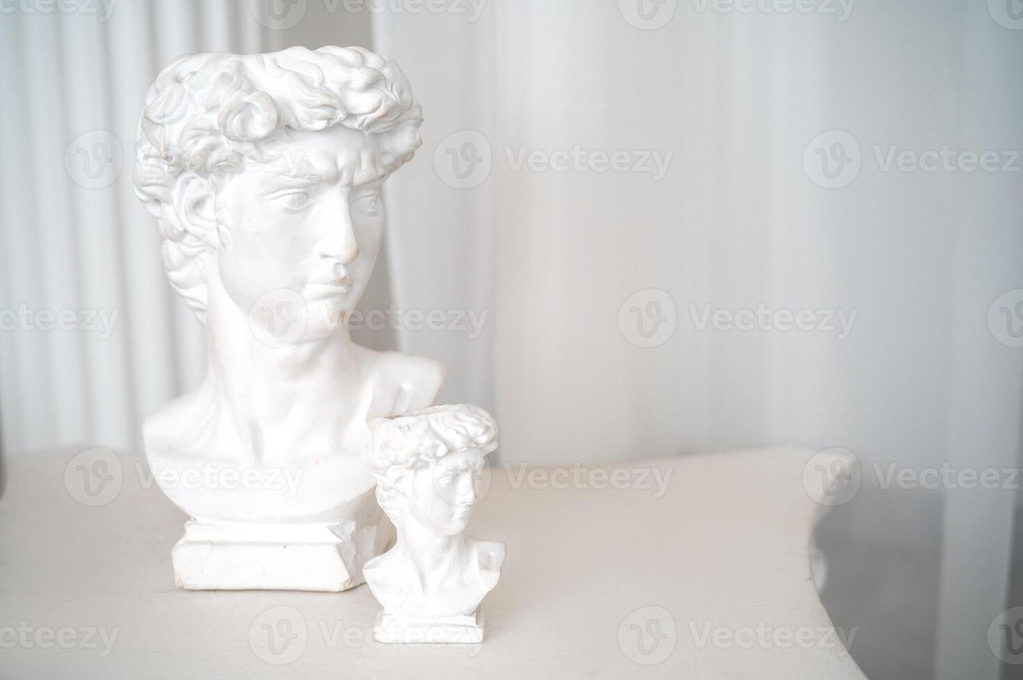 close up of beautiful antique decorative sculptures in interior. two plaster sculptures stand on antique style table. white chiffon fabric and columns behind. photo