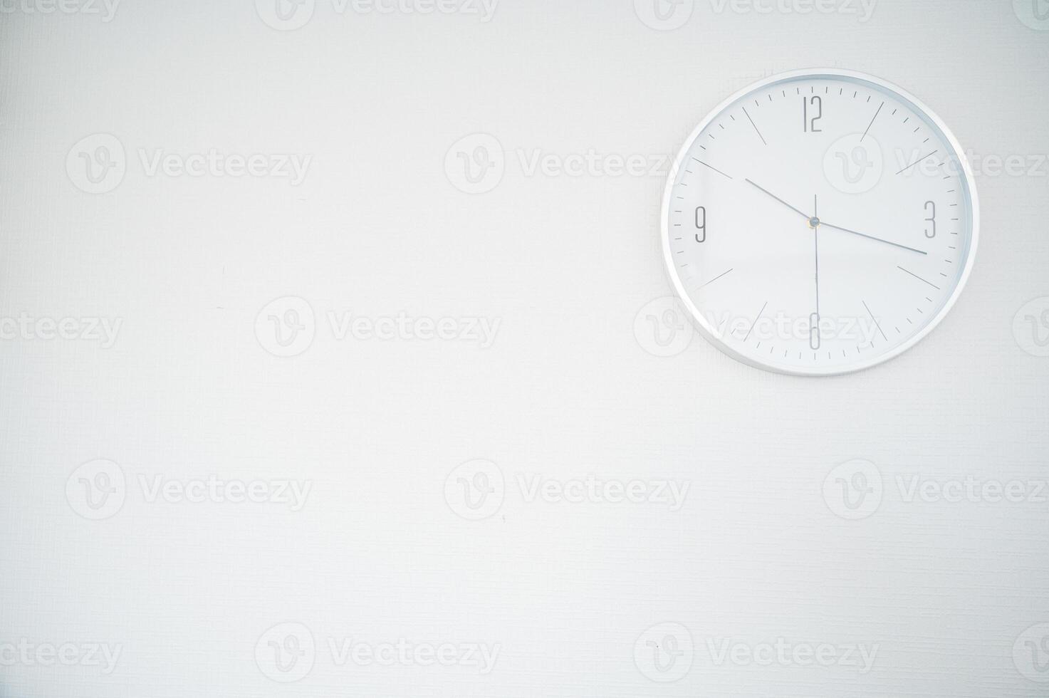 white round clock on a white wall. the clock is located in the upper right part. space for an inscription. the clock shows 10.18 photo