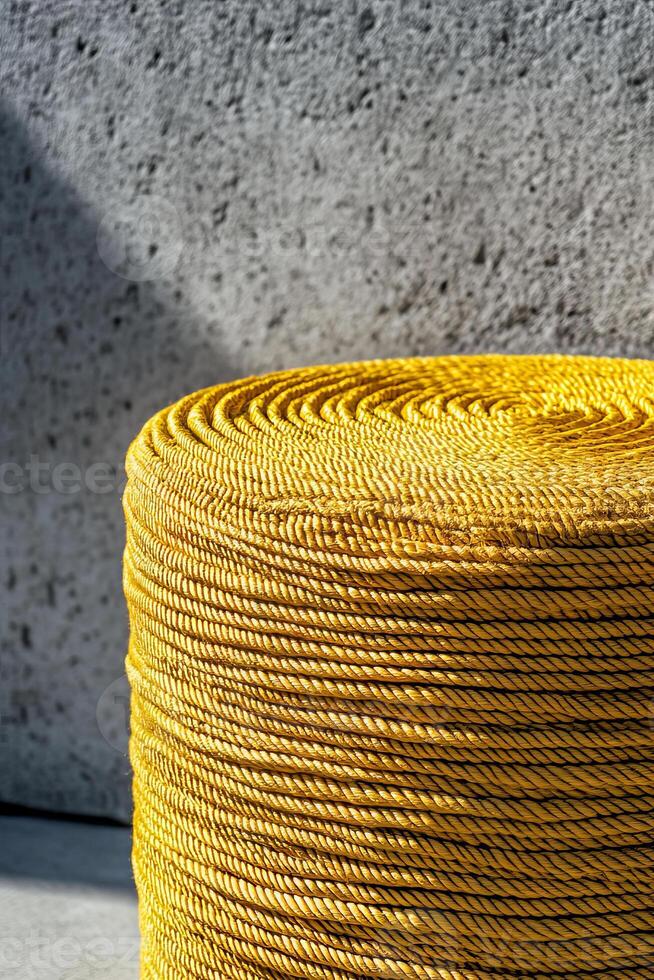 Bright yellow woven rope stacked in round shape against textured gray wall, creating vibrant contrast. sunlight enhances color and texture, adding depth to scene photo