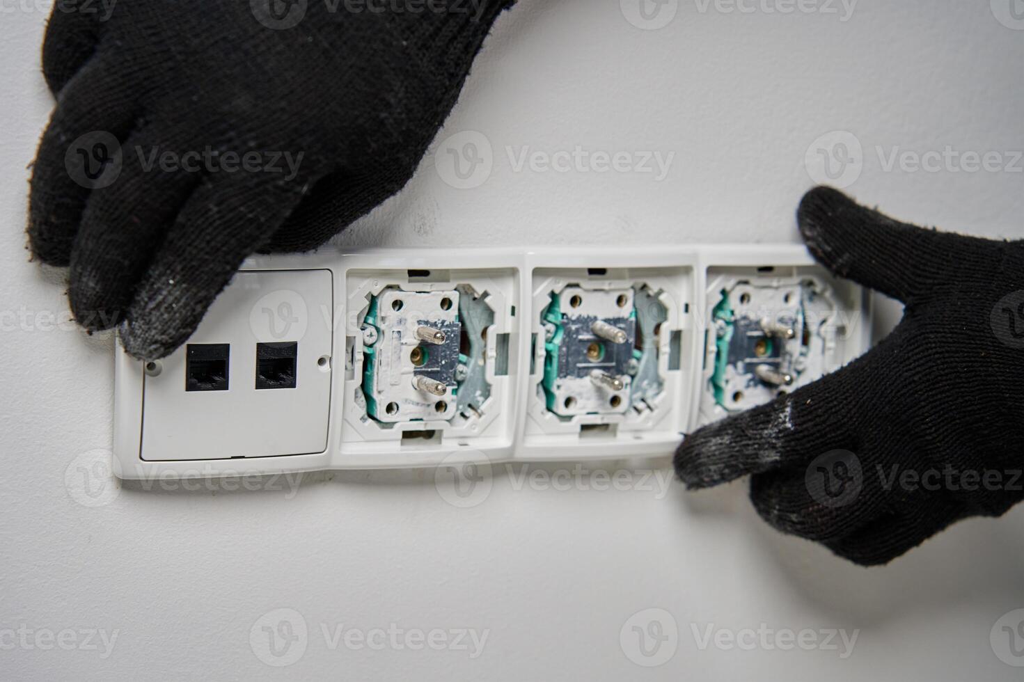 Close-up of an electrician wearing gloves installing power socket on white wall photo