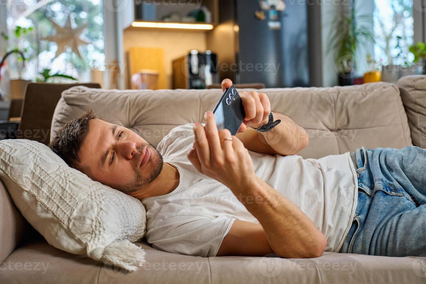 Man relaxing on couch using smartphone at home photo