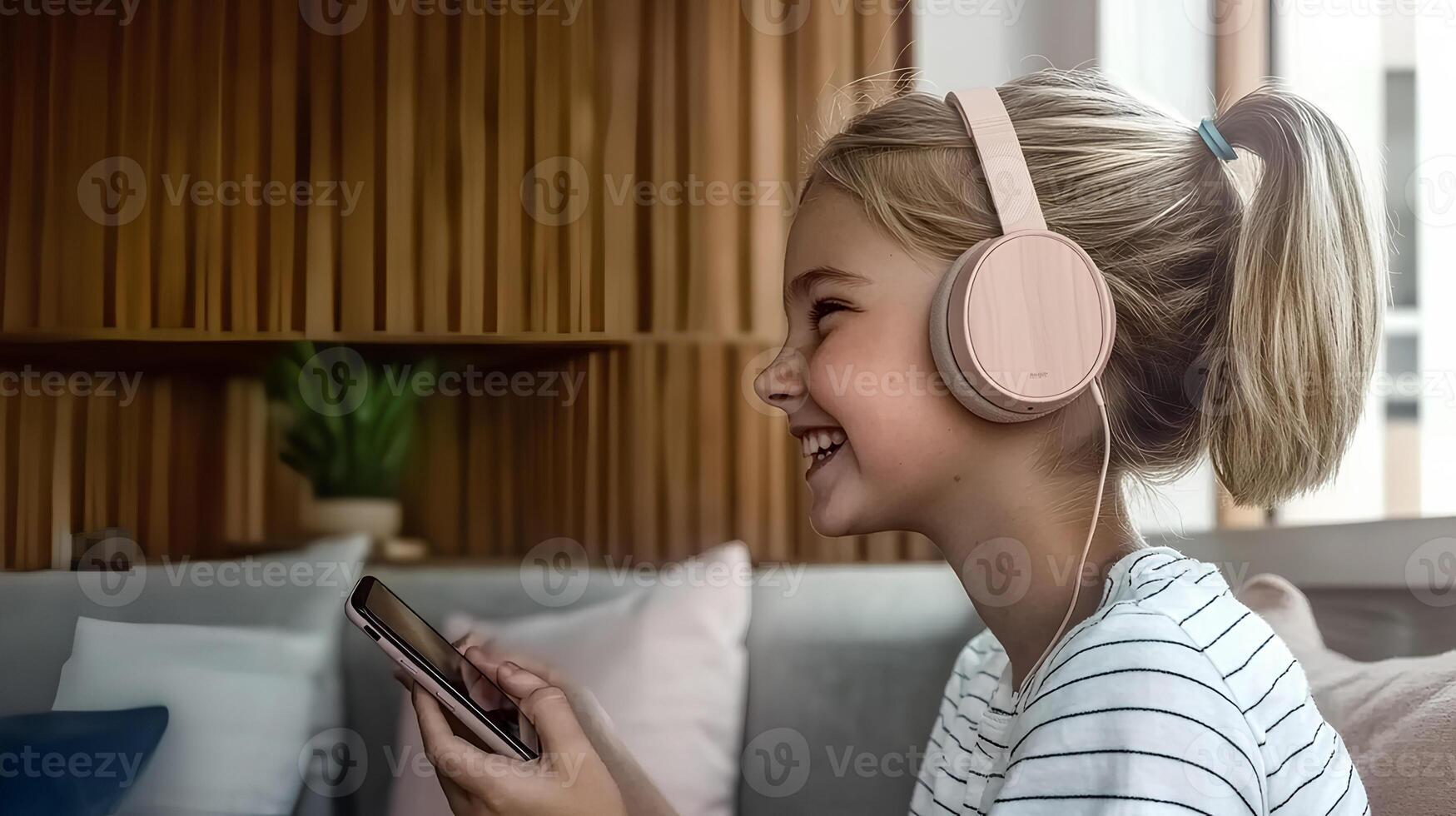 A joyful little girl wearing headphones, smiling while listening to music on her smartphone at home. photo