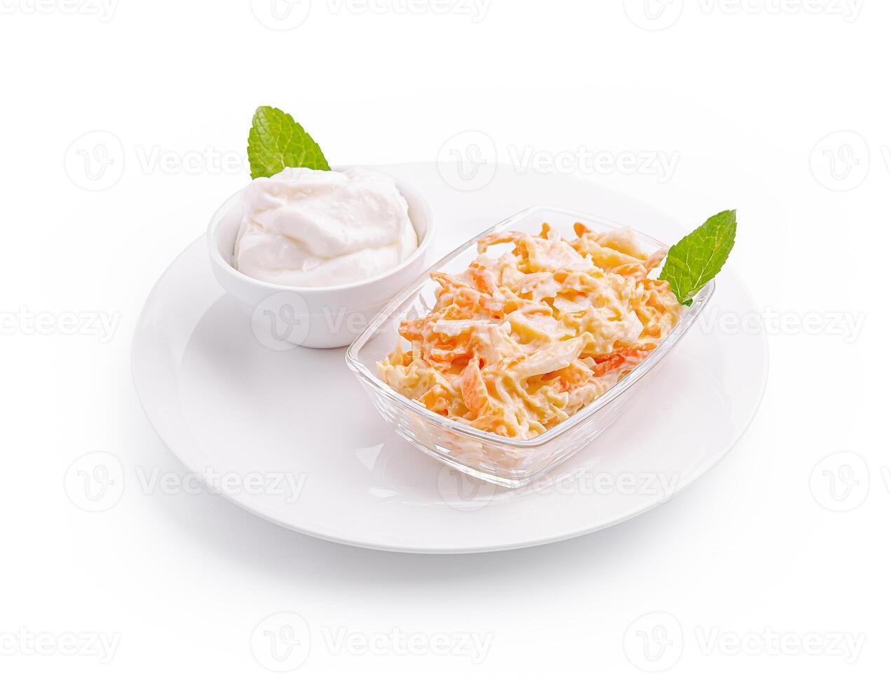 Fresh carrot salad with yogurt dressing served on a white plate with mint leaves at a kitchen table photo
