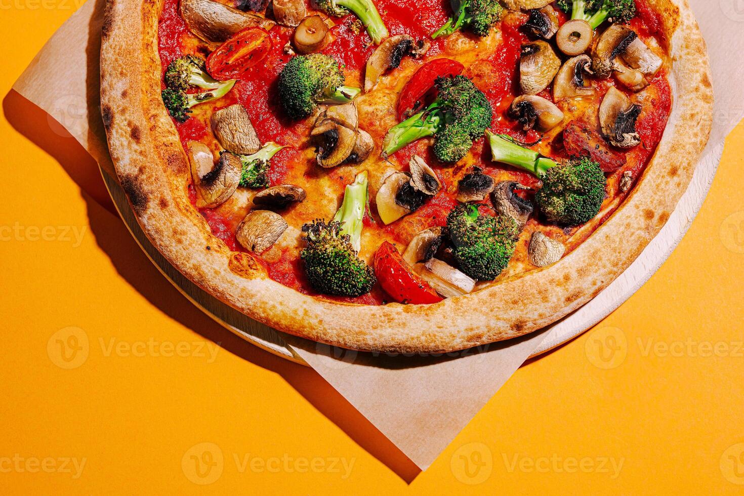 Delicious vegetable pizza topped with mushrooms, tomatoes, and broccoli on a vibrant yellow background photo