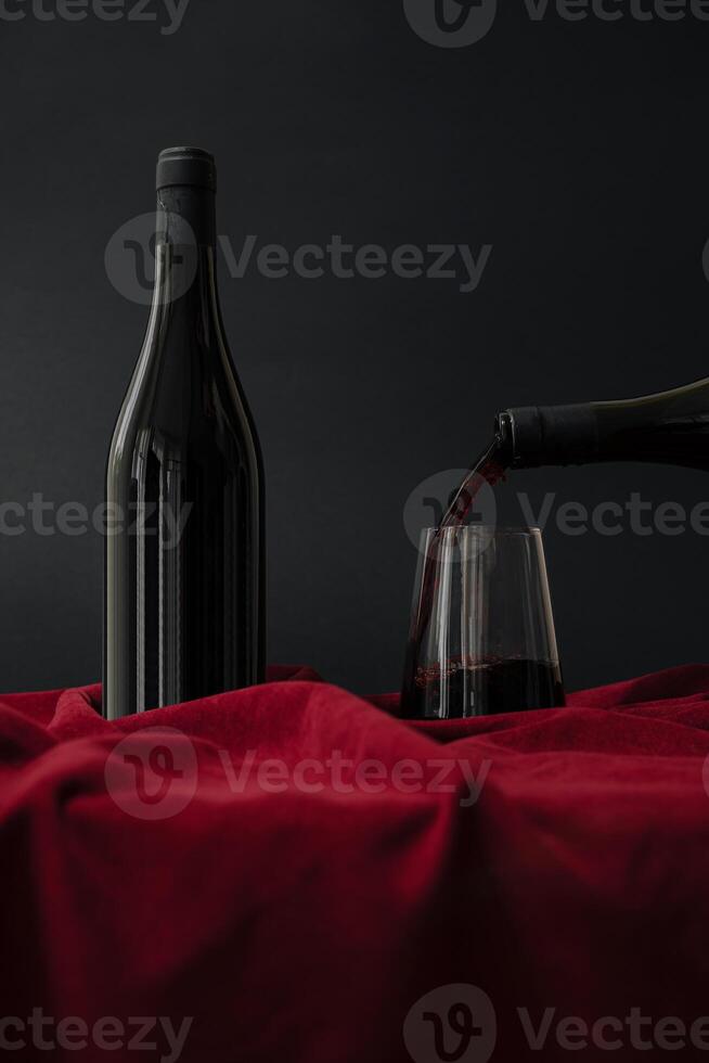 Pouring red wine from a bottle into a glass on a rich crimson cloth backdrop photo