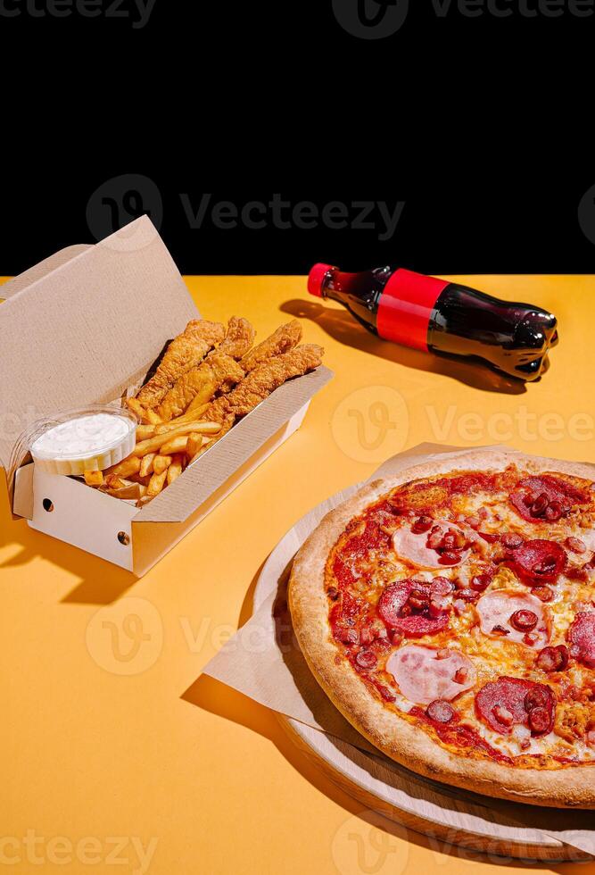 Delicious pizza, crispy chicken, and fries paired with soda create a perfect meal on a bright yellow table photo