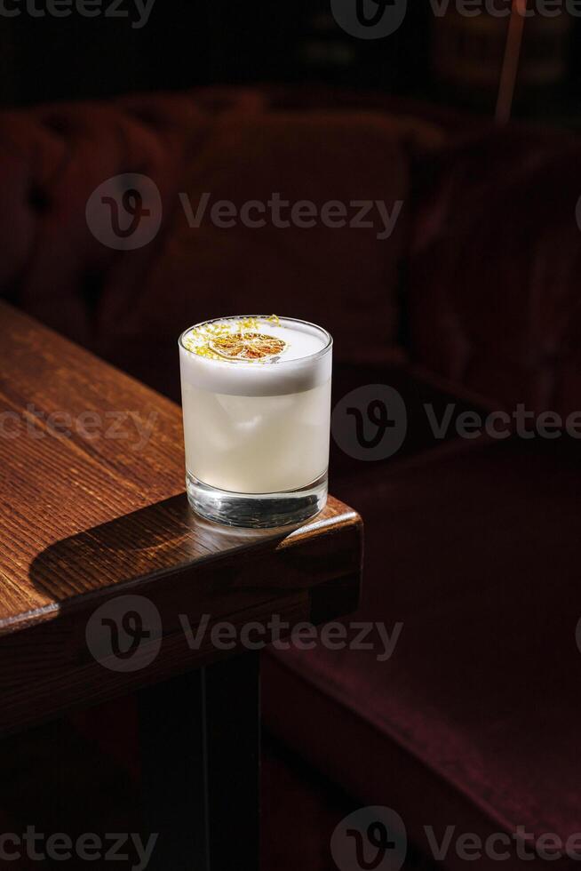 Refreshing cocktail sits on a wooden table beside a plush velvet sofa in a dimly lit lounge photo