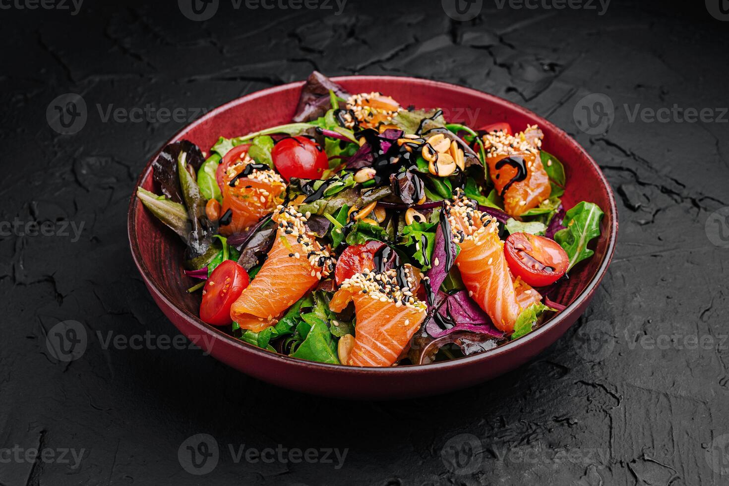 Fresh salmon salad featuring mixed greens, cherry tomatoes, and sesame seeds served in a red bowl on a dark textured background photo