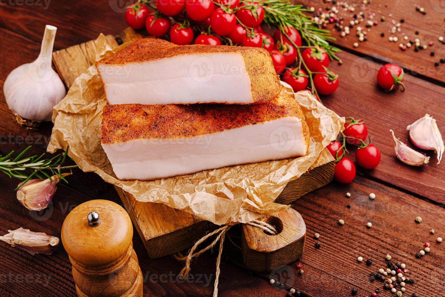Freshly cured pork belly with herbs, garlic, and cherry tomatoes on rustic wooden platter photo