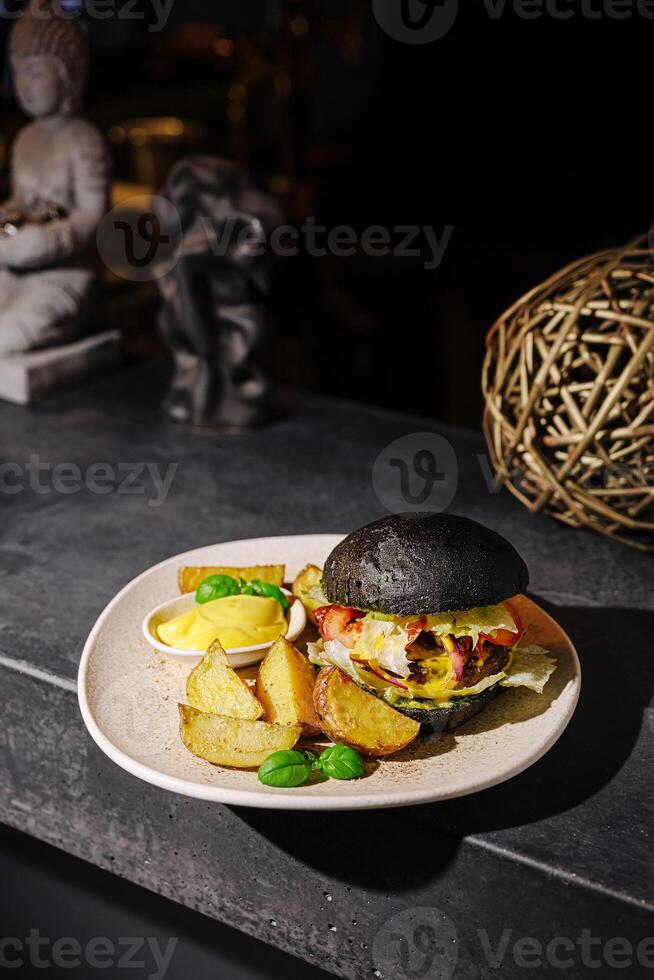 Gourmet burger with black bun and crispy potatoes served in a cozy restaurant setting at night photo