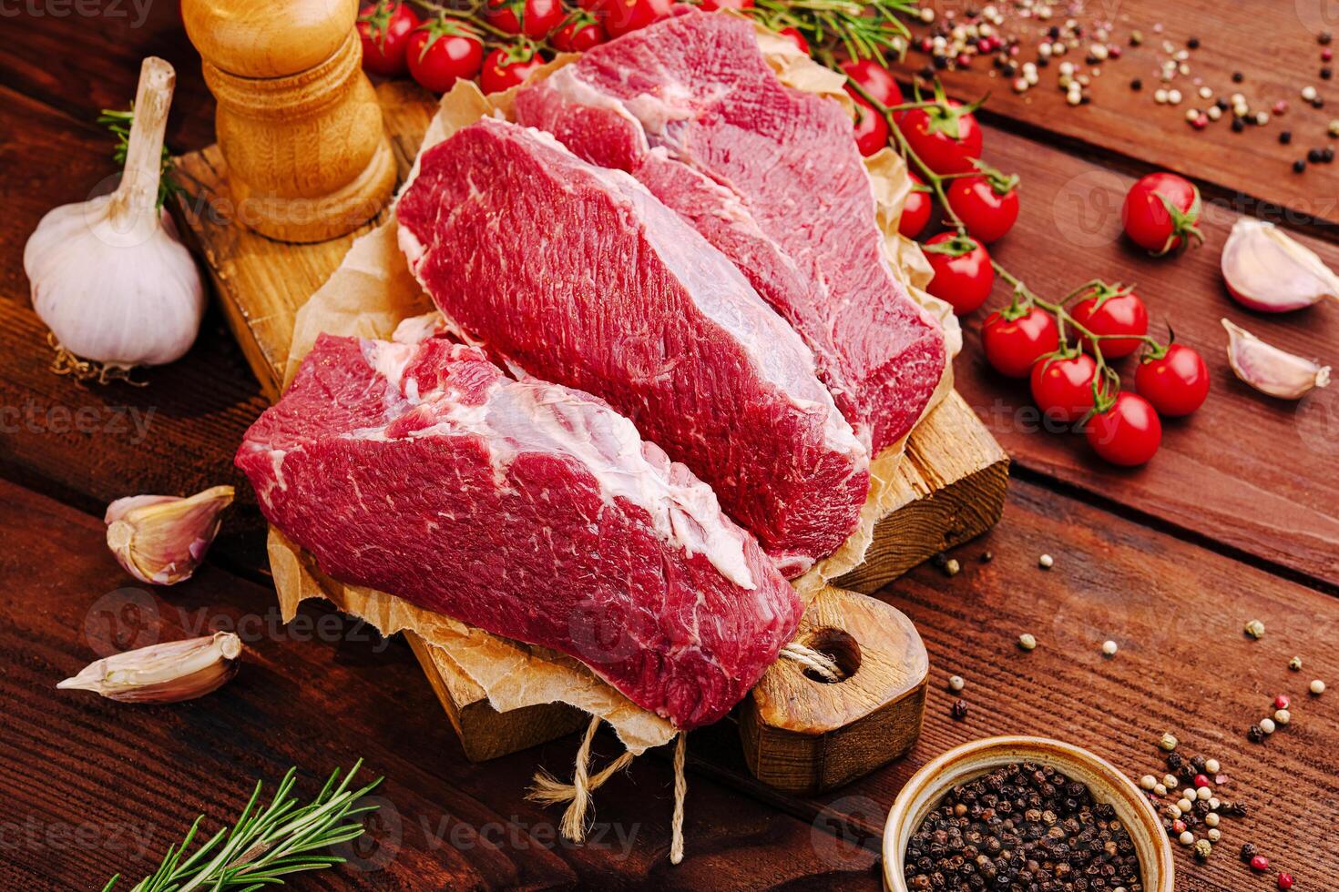 Fresh cuts of beef on a wooden board with herbs and garlic in a rustic kitchen setting photo