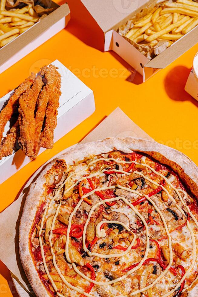 Delicious pizza with toppings served alongside crispy fries and chicken tenders on a vibrant orange background photo