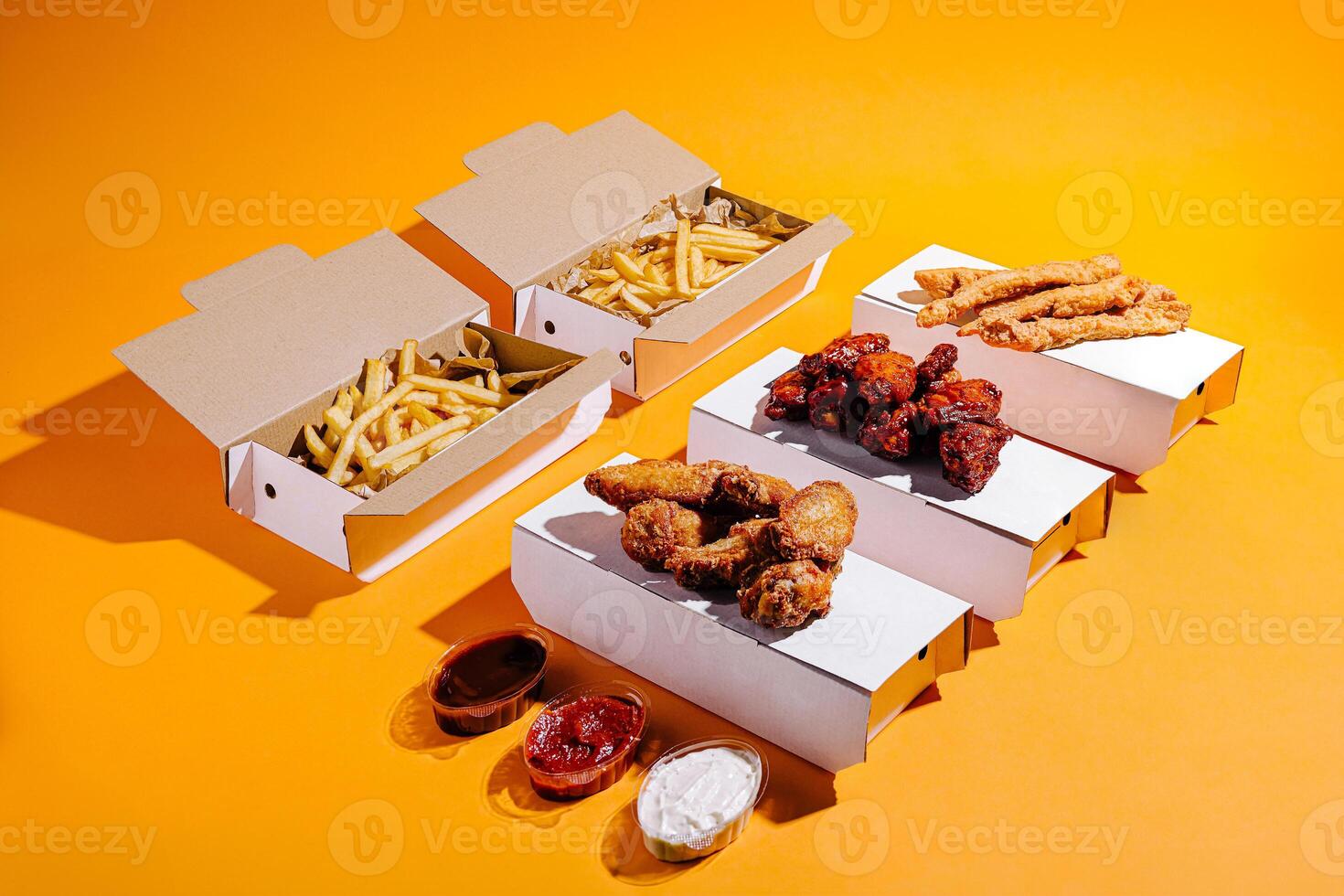 Fried chicken and crispy fries served in takeout boxes on vibrant orange backdrop photo