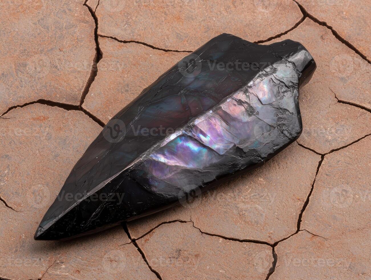 A polished obsidian arrowhead on a cracked surface photo