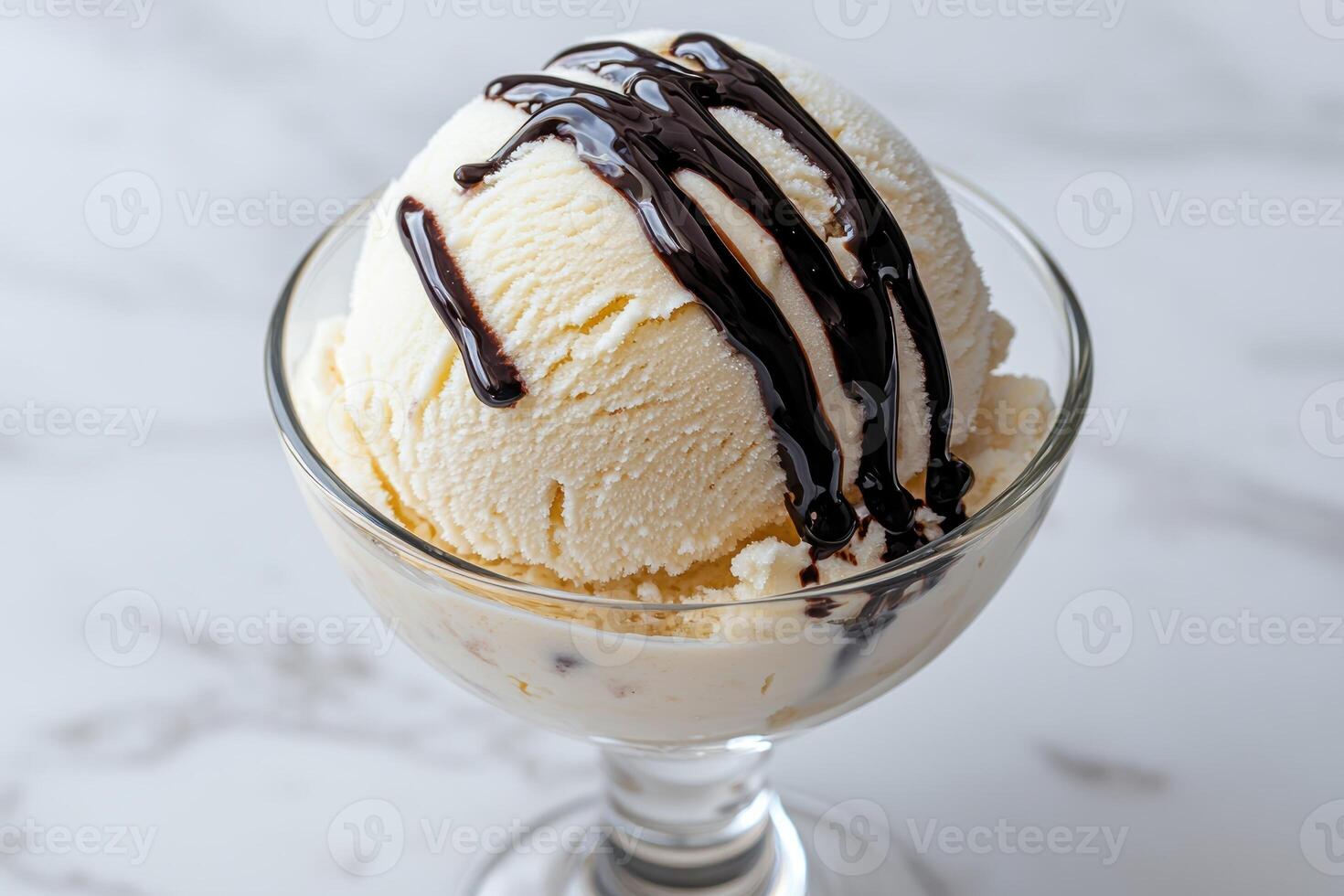 A scoop of vanilla ice cream with chocolate sauce in a glass bowl photo