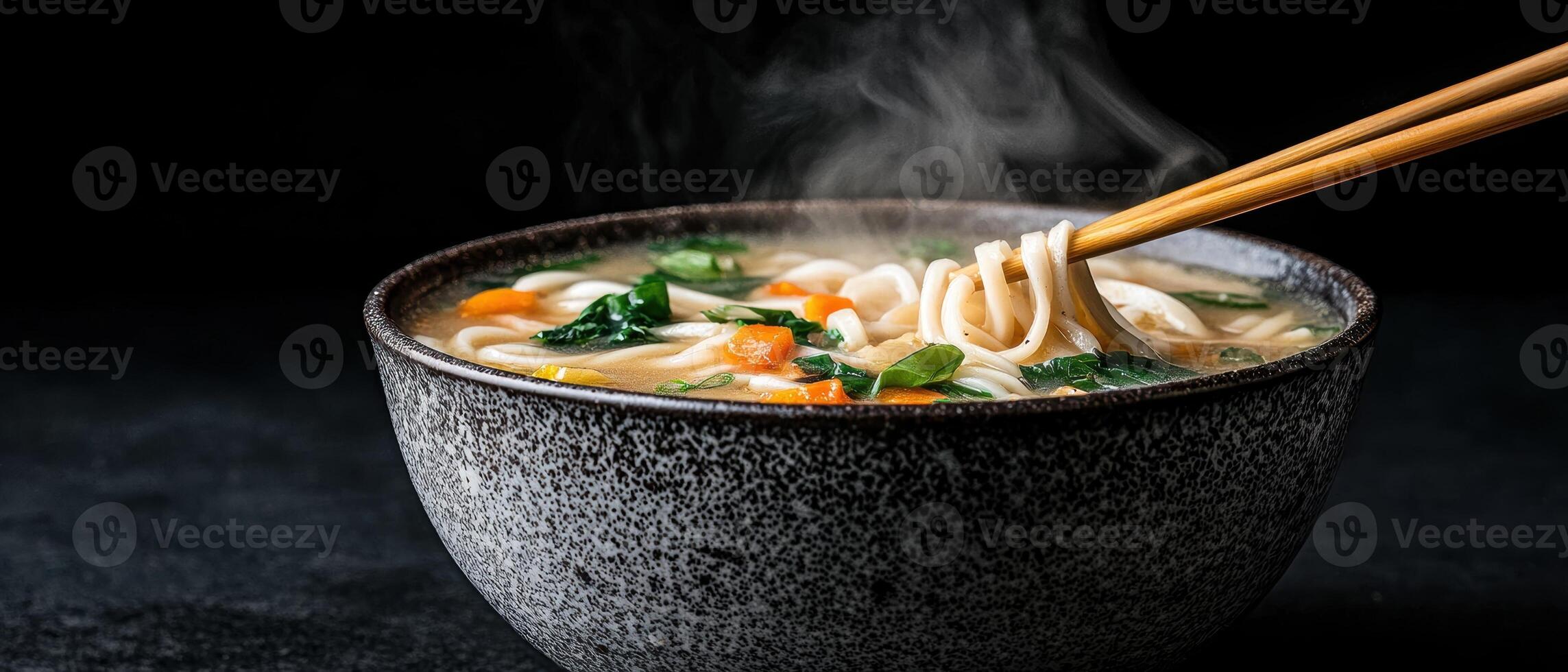 A steaming bowl of noodle soup with vegetables being lifted with chopsticks photo