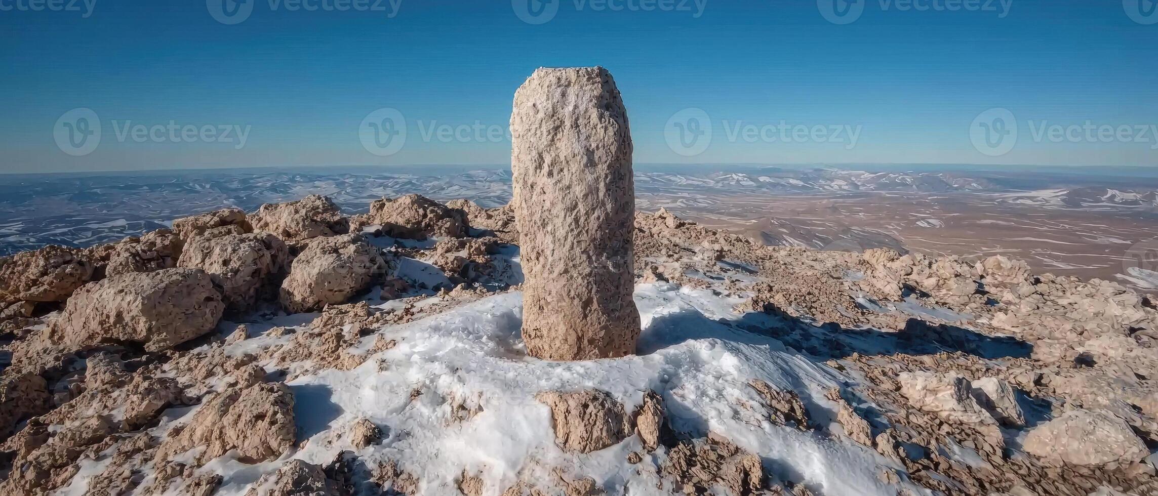 Stone pillar on a snowy mountain peak overlooking a vast landscape photo
