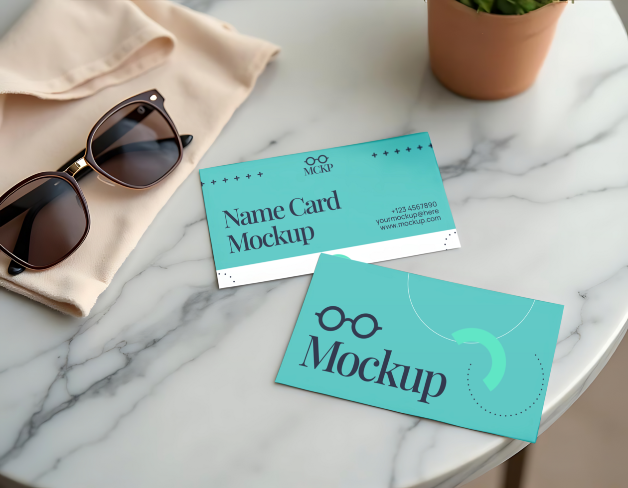 Two teal name card mockups rest on a marble table next to sunglasses and a folded piece of fabric psd
