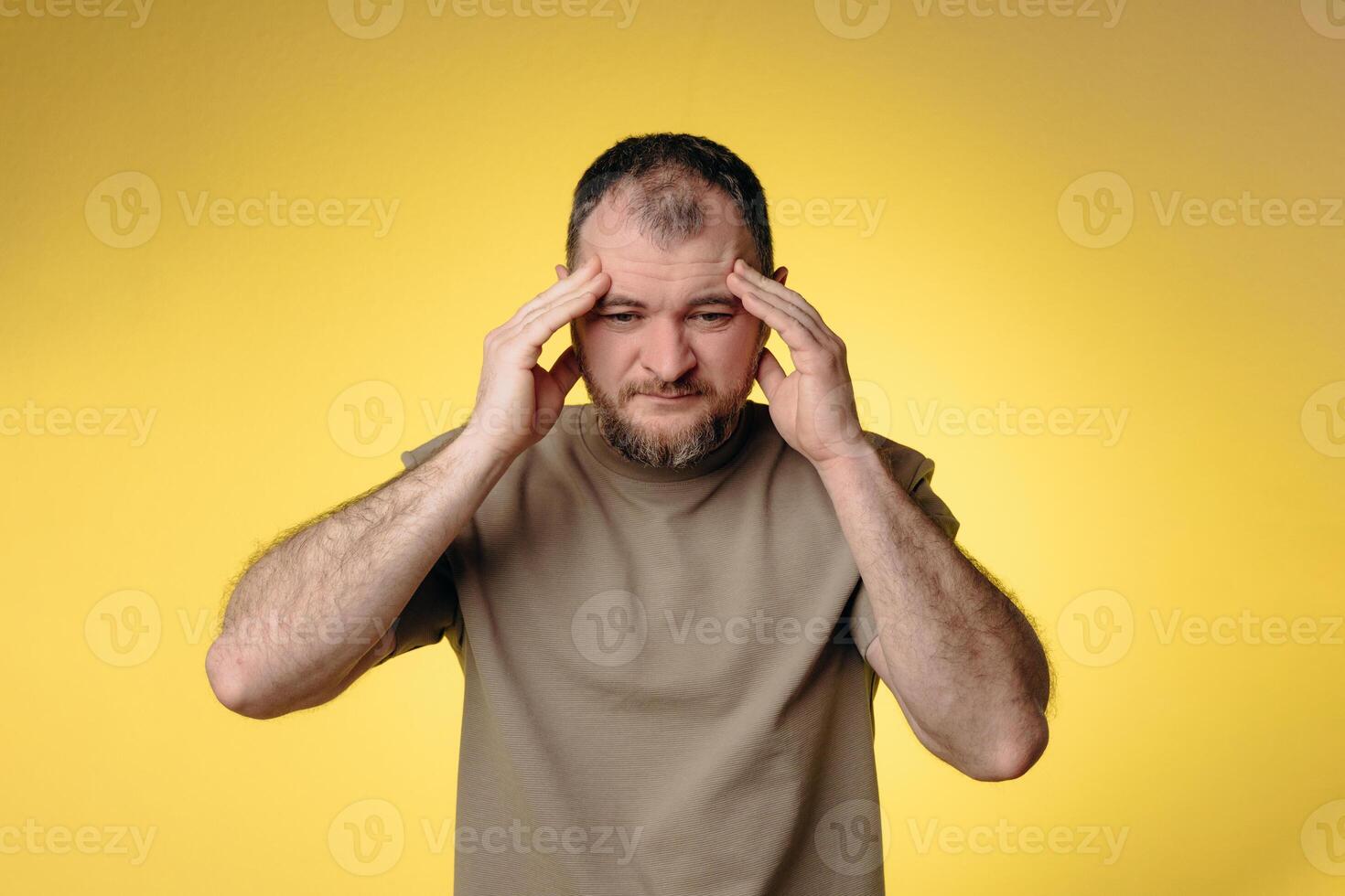 A man has a severe headache. He holds his head with his hands and massages his temples to relieve the pain in his head. Overwork and fatigue lead to migraines. The headache prevents him from thinking. photo