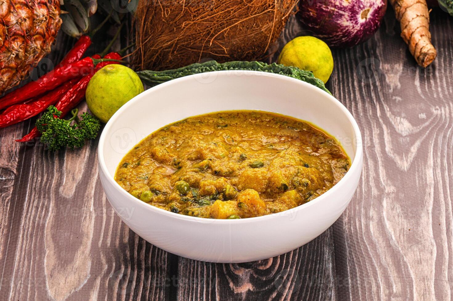 A bowl of soup sitting on a table next to a bunch of vegetables photo