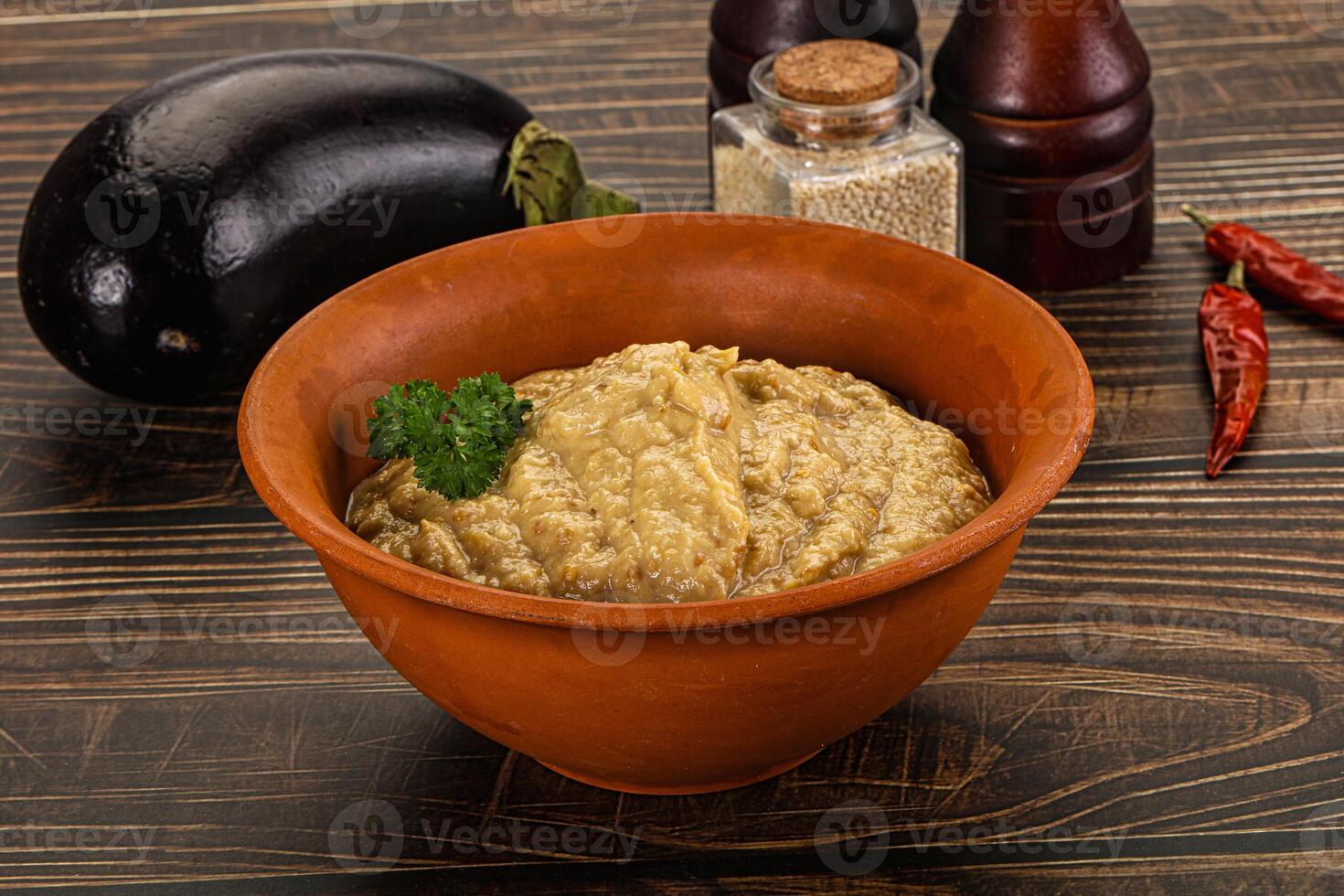 A bowl of eggplant dip with a pepper and a bottle of chili photo