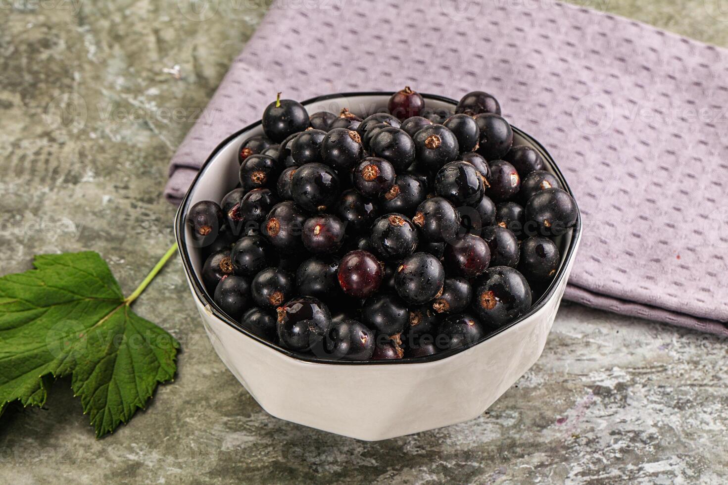 A bowl of black currants with leaves on a table photo