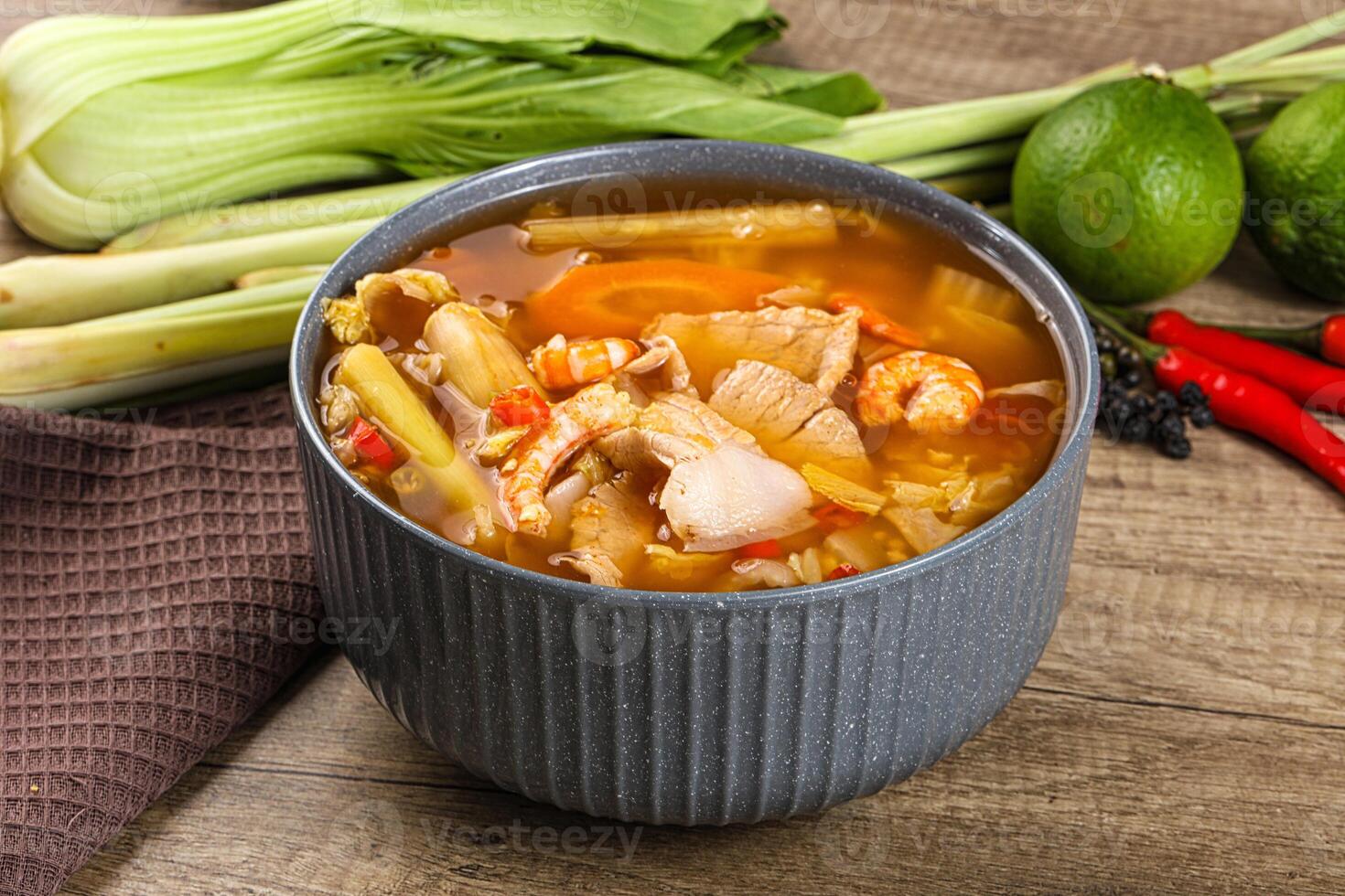 A bowl of soup with vegetables and meat on a wooden table photo