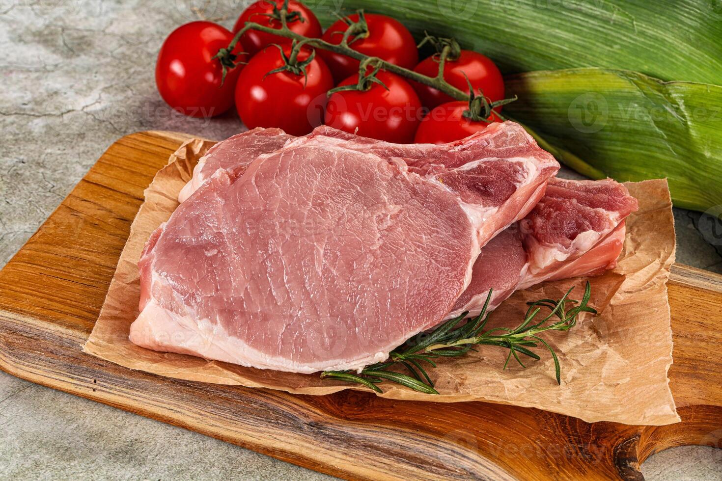 Raw pork on a cutting board with tomatoes and corn photo