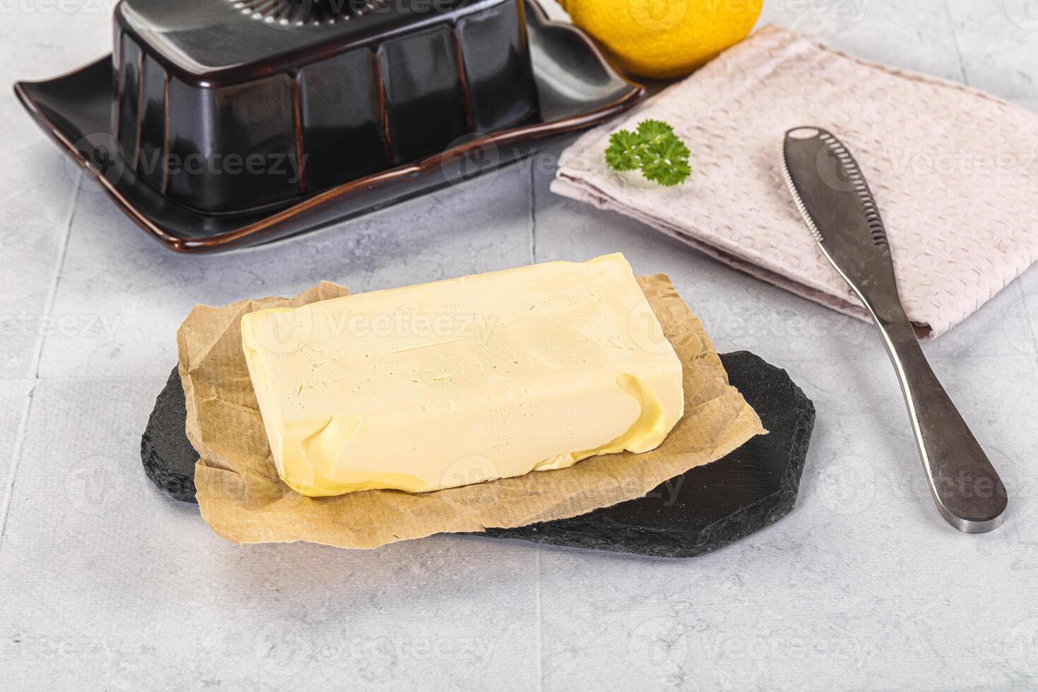 A butter block on a cutting board next to a knife and a lemon photo