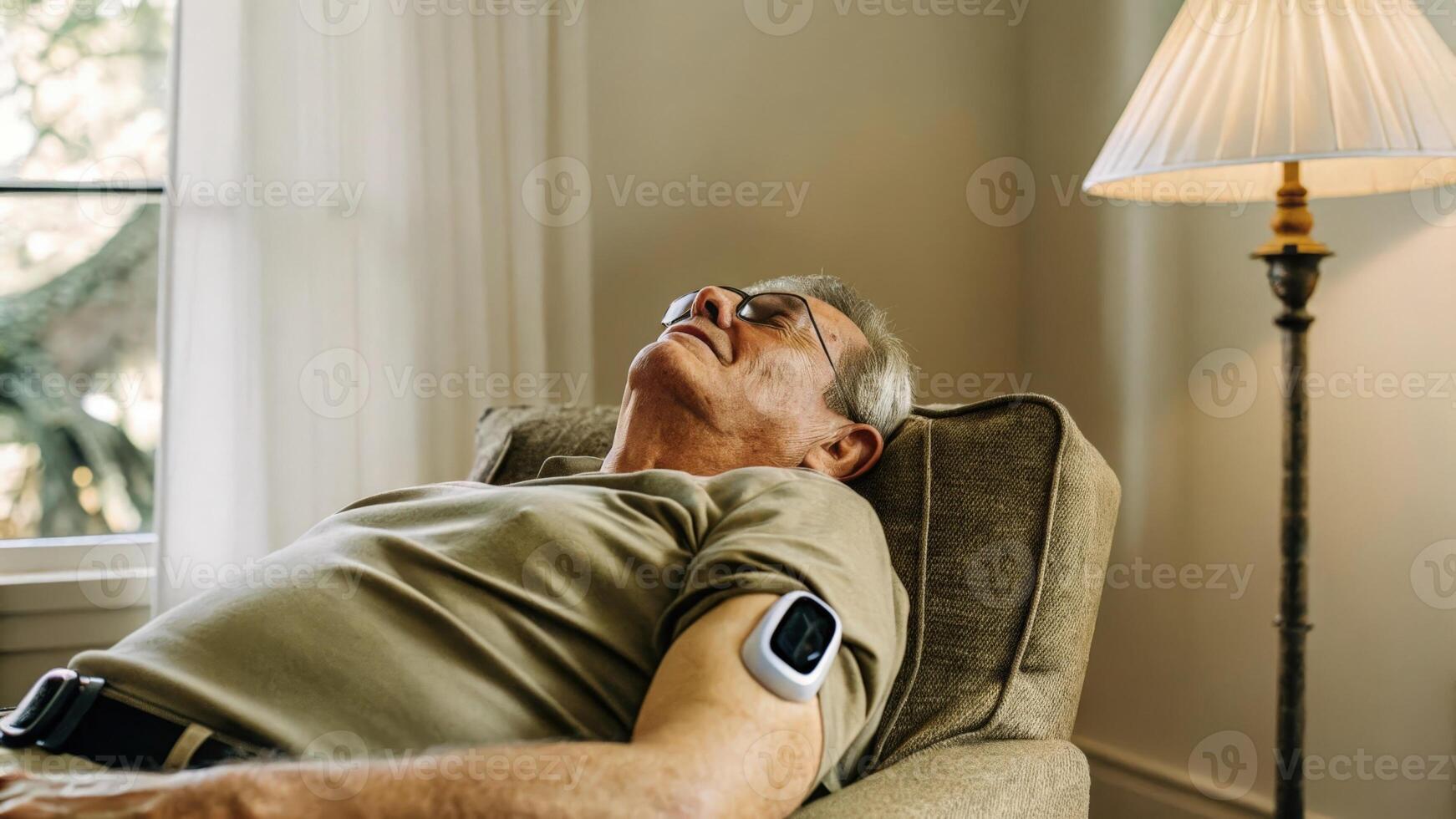 A senior man relaxing in a chair with a smart patch on his upper arm that displays oxygen saturation levels illuminated by soft ambient light from a lamp nearby.. photo