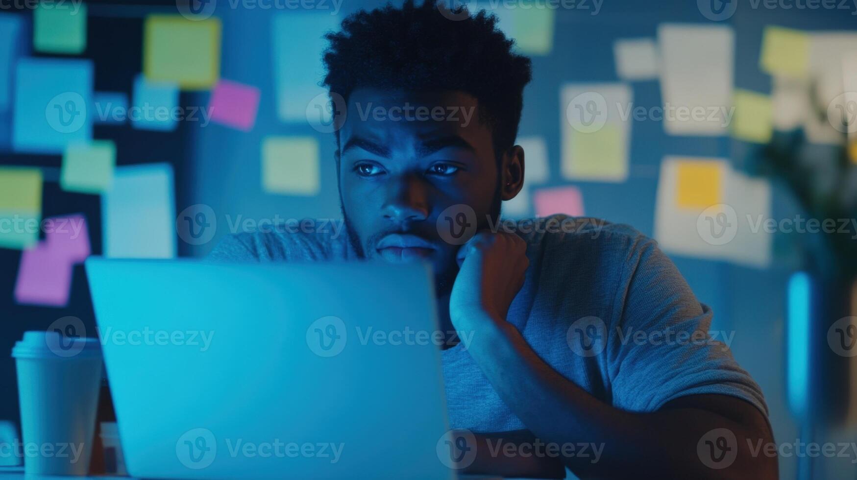 A concentrated face illuminated by the blue light of a laptop showcasing a participant deep in thought surrounded by coffee cups and sticky notes filled with brainstorming ideas an photo