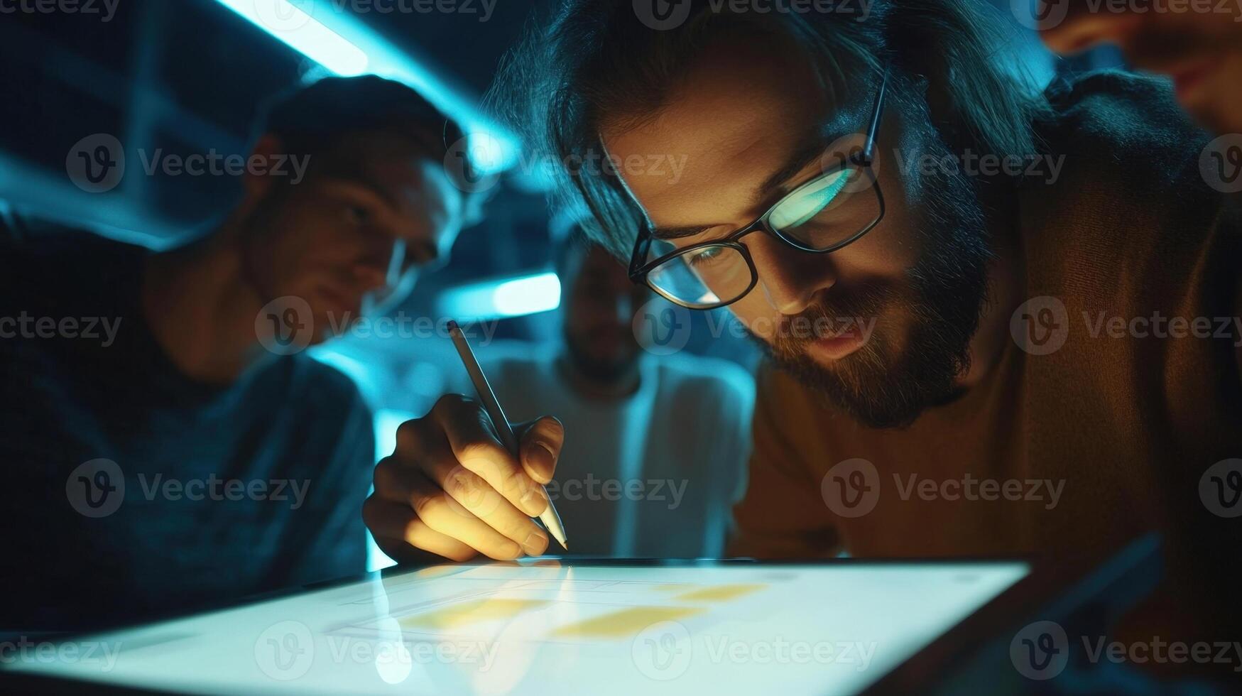 A medium closeup reveals a focused team member sketching a prototype interface on a digital tablet illuminated by soft overhead lights as colleagues lean in their expressions reflectin photo