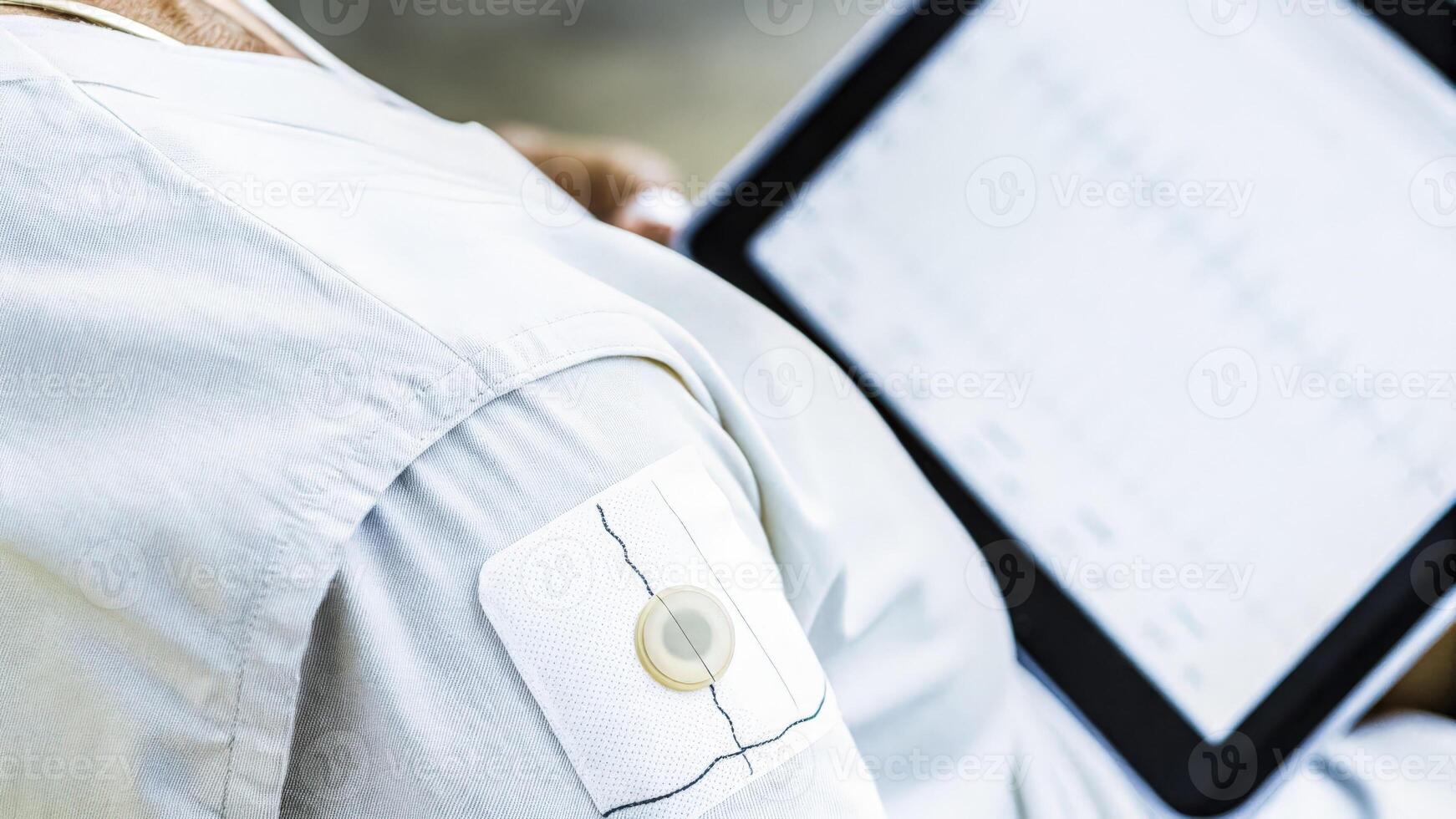 A closeup shot of an advanced chest patch sensor adhered to the skin of an older adult capturing electrical signals with clear visual feedback on a nearby digital tablet.. photo