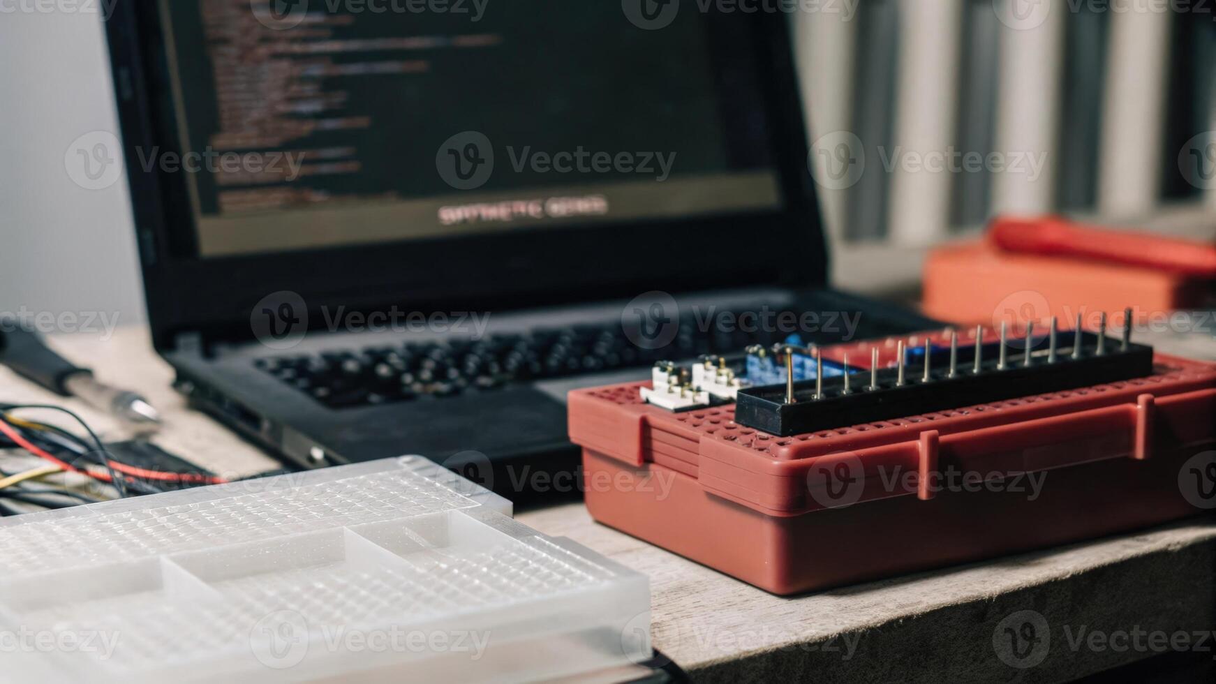 An organized workspace featuring various small circuit components wires and microcontrollers alongside a laptop displaying code for programming synthetic genes.. photo