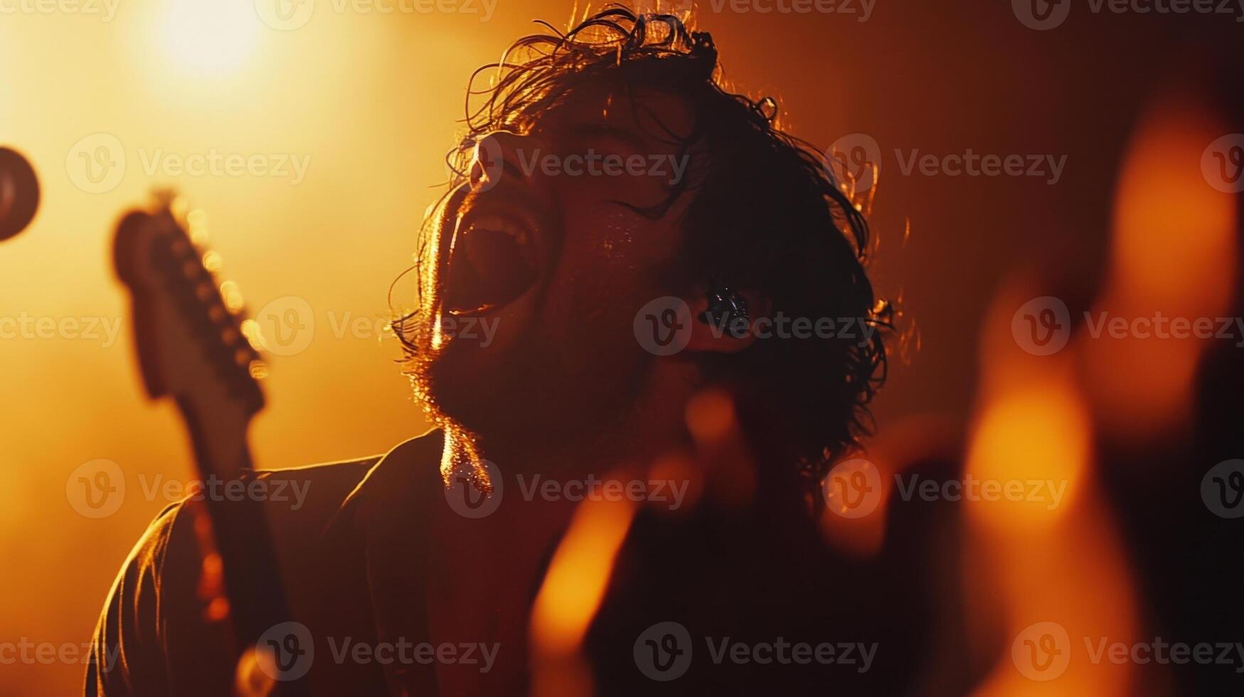 A dynamic shot of a lead singer passionately belting out a song with the camera focused on their electrifying presence while the audience is faintly visible their hands raised in photo