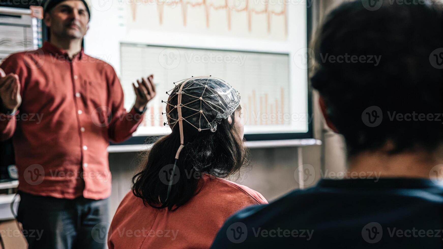 A researcher demonstrating a neurofeedback exercise to a small group with electrodes p on a participants head visually portraying the intersection of technology and human. photo